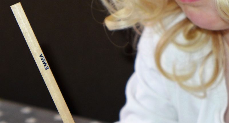 child holding pencil crayon with name on